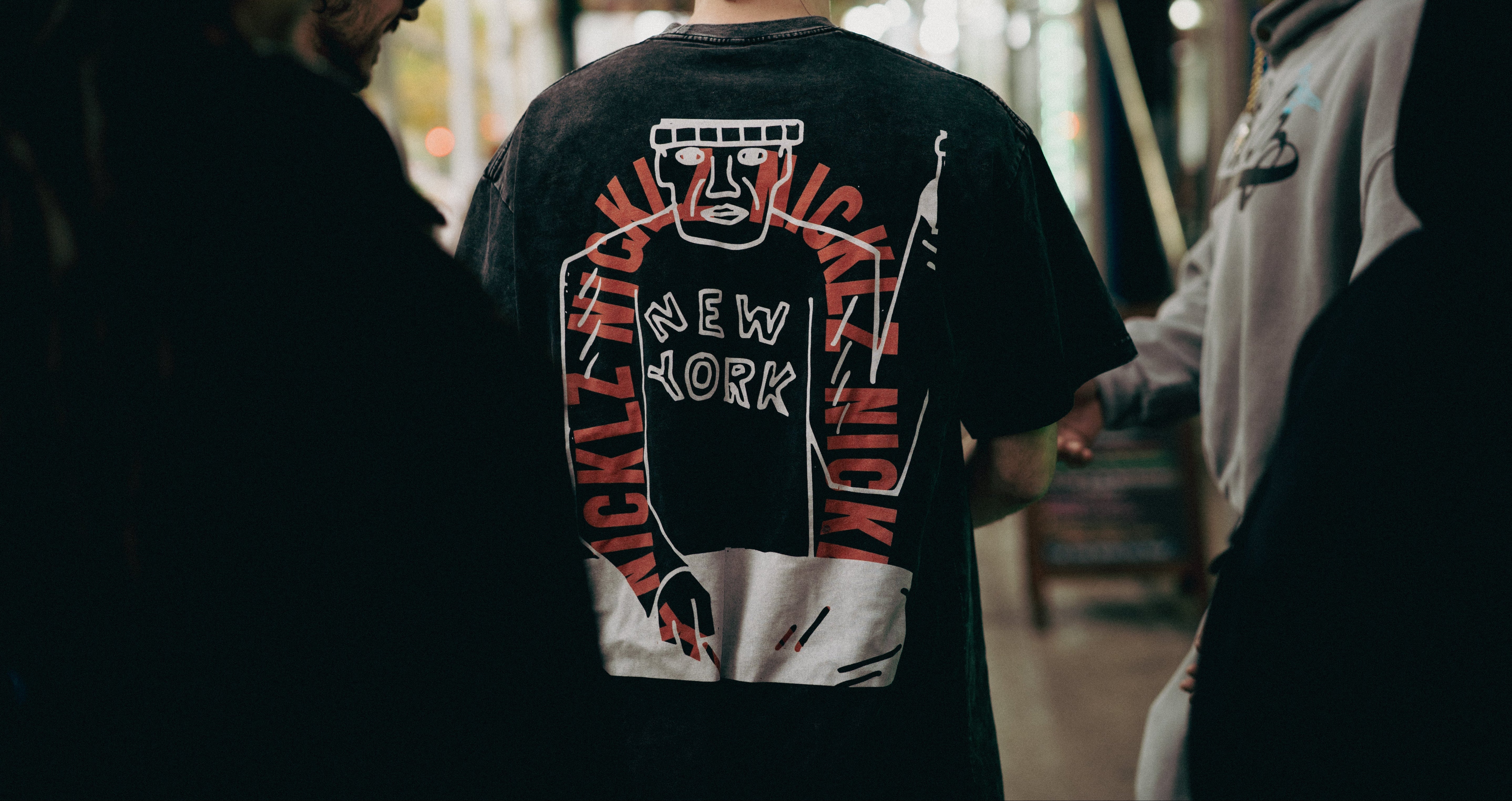 Person wearing a black t-shirt with a graphic design on the back, standing in an urban setting.

