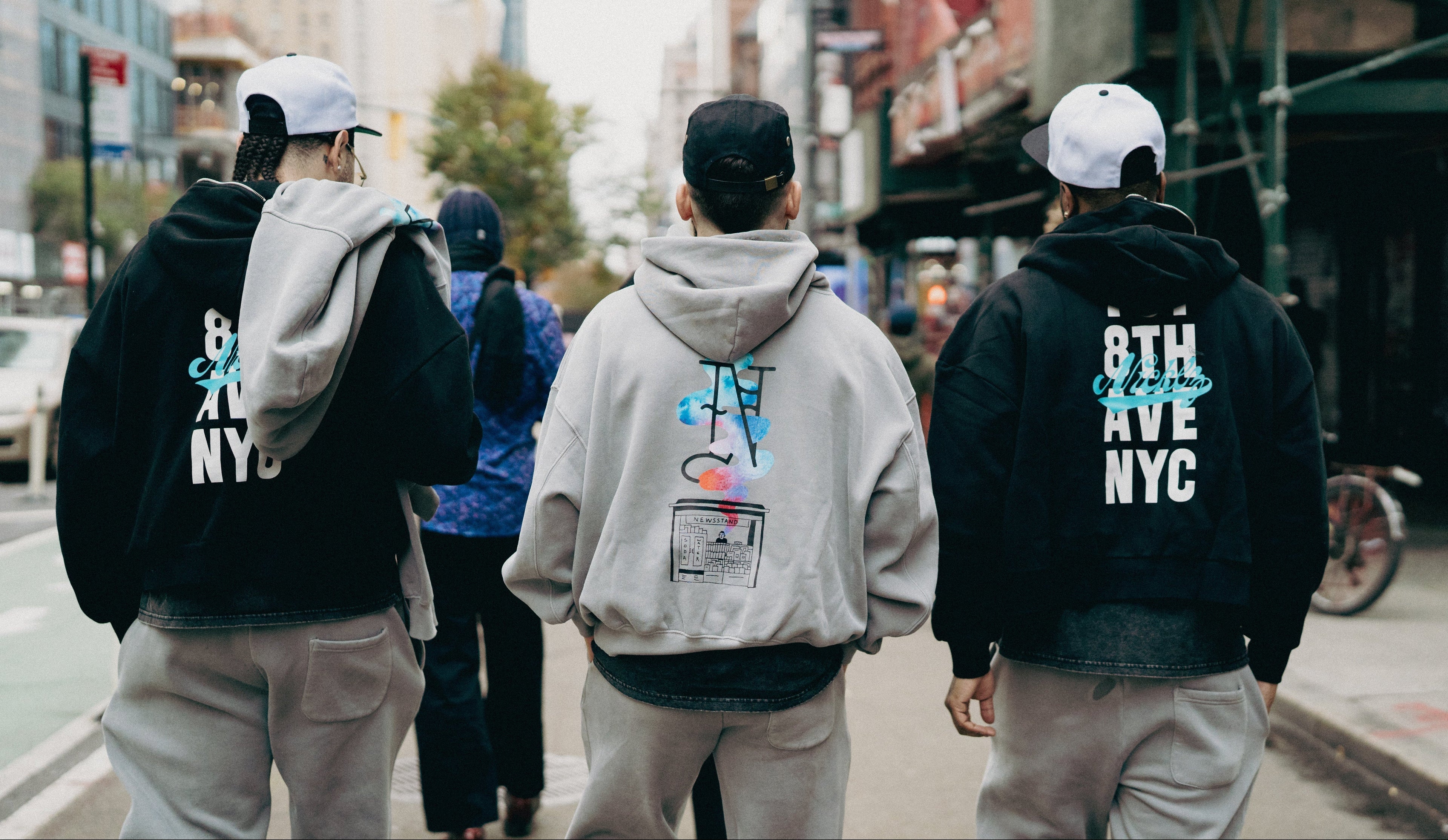 Three people walking on a city street, wearing hoodies with text and graphics.

